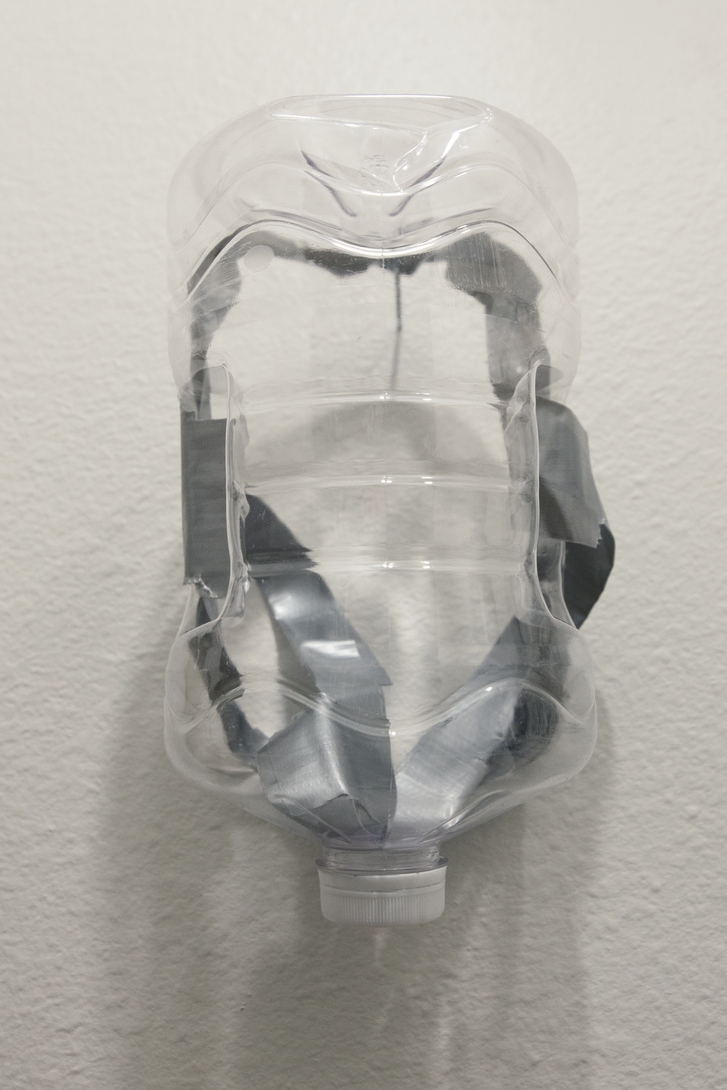 A clear plastic jug fashioned into a face mask hung on a white wall